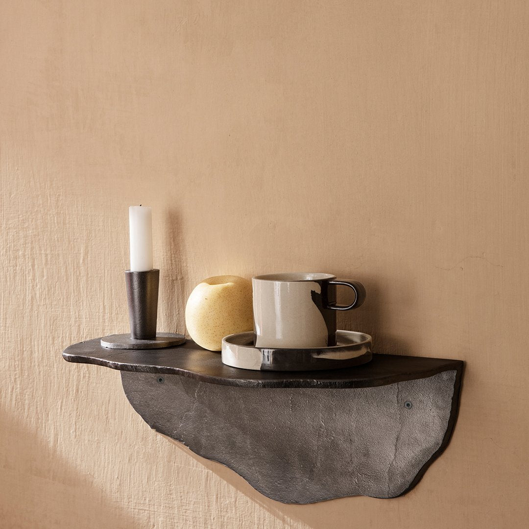 Black shelf against a beige wall, featuring a white candle, yellow fruit, and black and white dishware.