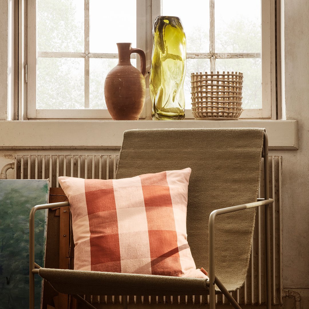 "Decorative pillow with a red and white checkered pattern, placed on a neutral-colored chair in a cozy indoor setting."