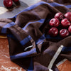 Brown plaid fabric with blue stripes, paired with dark red plums on a marble surface.