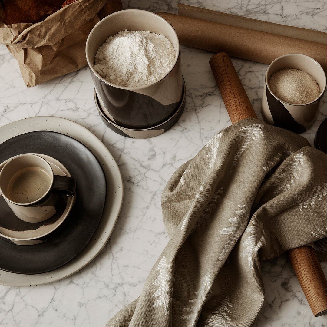 Elegant beige and dark brown tableware with a subtle floral pattern on a marble countertop, complemented by baking tools.