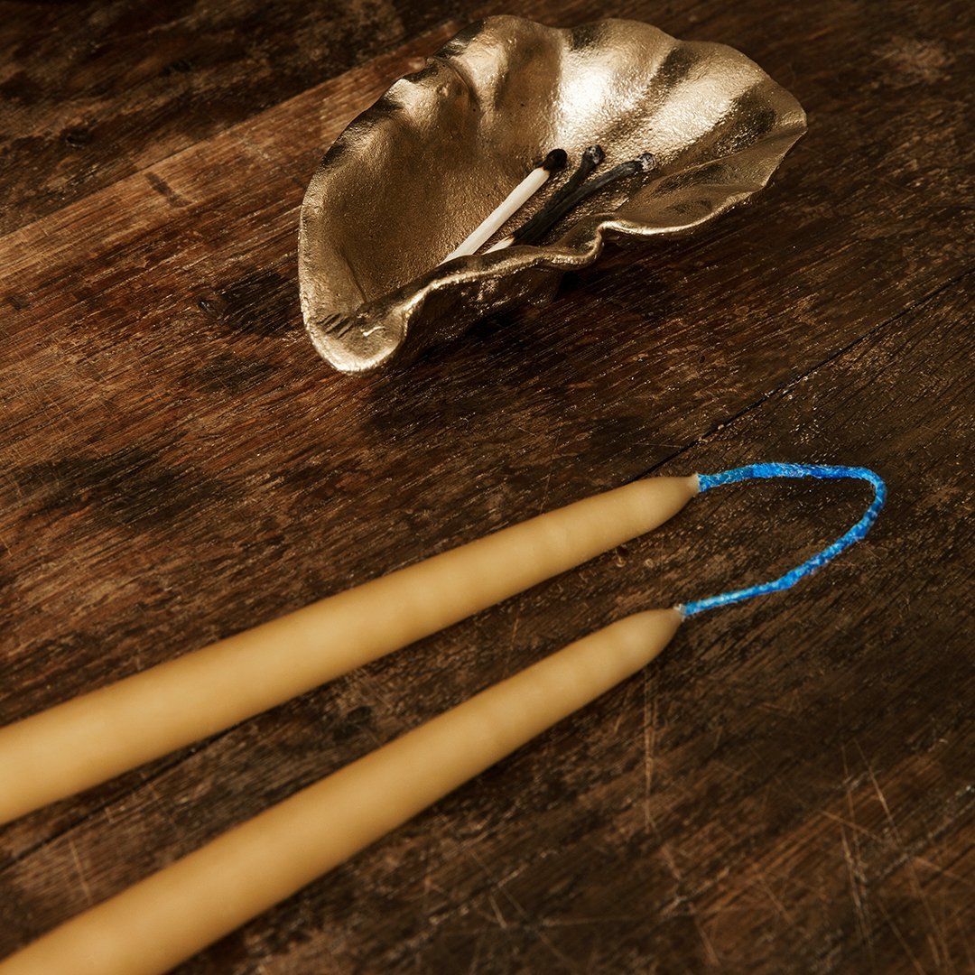 "Beeswax candles in natural beige with blue detailing, paired with a decorative silver shell on a wooden surface."