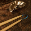 "Beeswax candles in natural beige with blue detailing, paired with a decorative silver shell on a wooden surface."