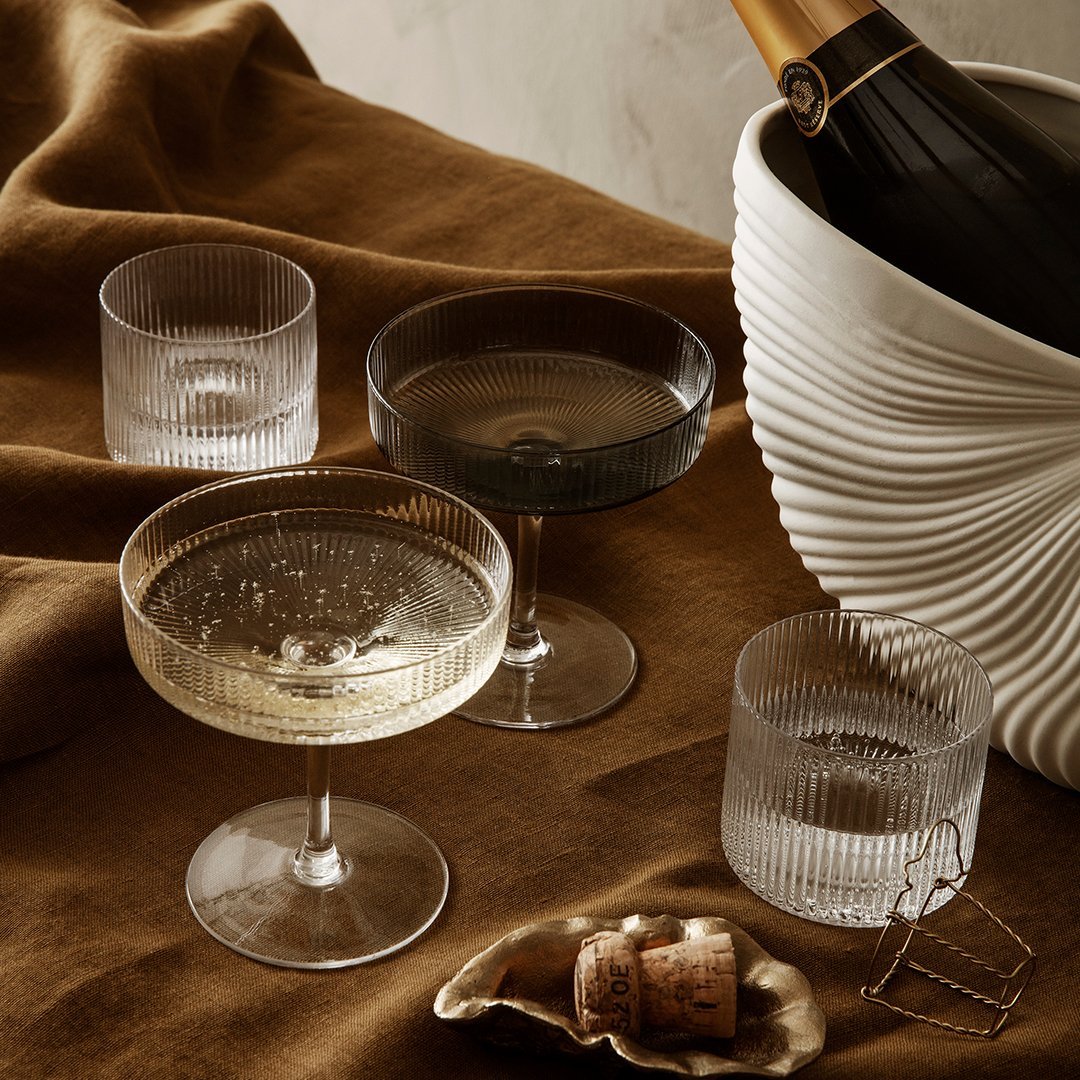 Elegant glassware set featuring clear, frosted, and black ribbed designs on a warm, textured brown tablecloth.
