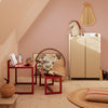 Red accent tables, beige cabinet, soft pink walls, patterned artwork, and textured natural materials create a cozy space.
