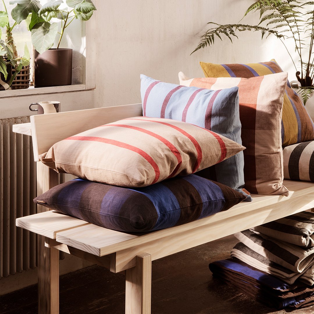Colorful cushions featuring stripes in beige, blue, brown, and terracotta arranged on a wooden bench.