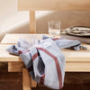 Light blue fabric with deep red diagonal stripes draped on a wooden table. Minimalistic and modern design.