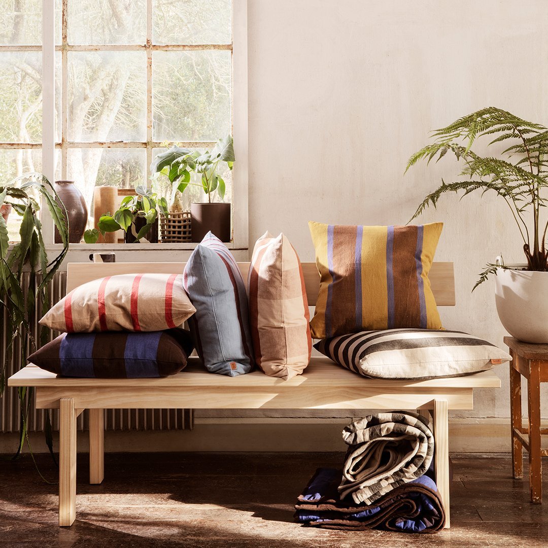 Multicolored striped cushions in shades of blue, brown, and yellow arranged on a wooden bench.