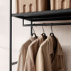 Neutral beige coats hanging on a black rack, with textured tan storage bins above. Minimalist and modern aesthetic.