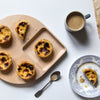 Wooden tray with golden pastries, blue floral plate, and a gray mug with coffee on a white background.