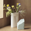 White ribbed vase with colorful wildflowers, accompanied by a textured light blue stone. Modern, minimalistic design.