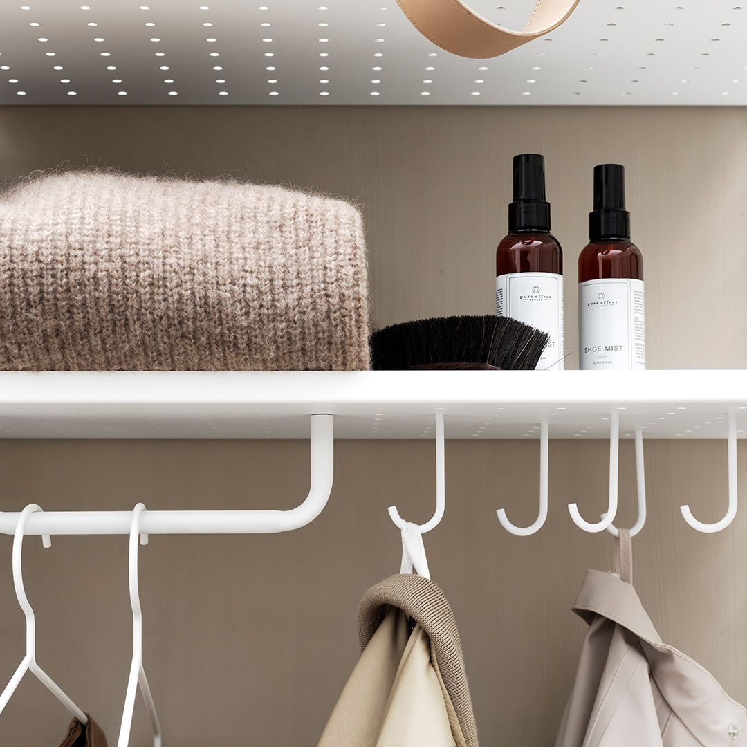 Cozy beige knit blanket on a white shelf, with brown and black spray bottles and a beige coat hanging below.