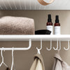 Cozy beige knit blanket on a white shelf, with brown and black spray bottles and a beige coat hanging below.